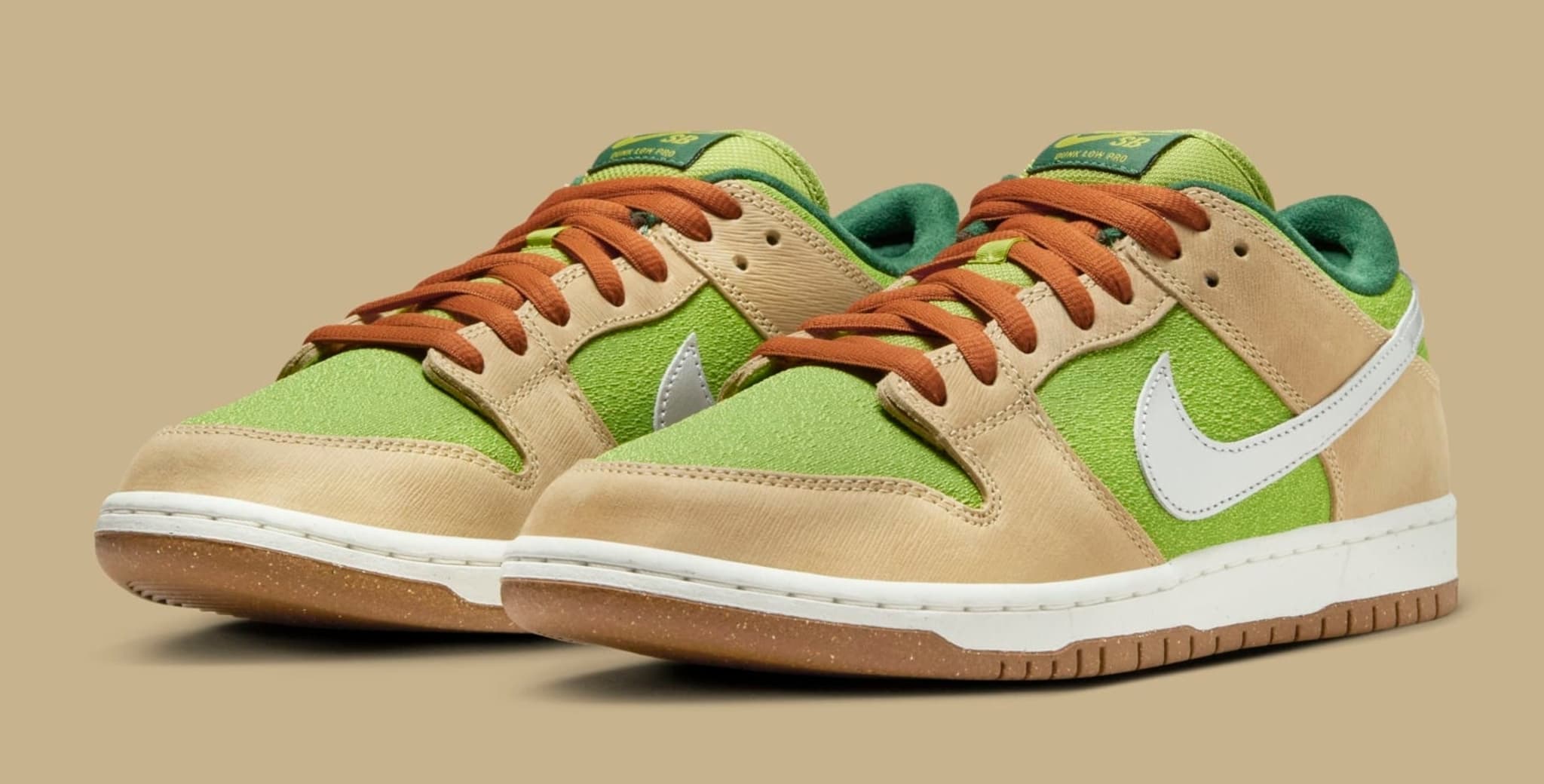 Nike Dunk Low sneakers with green and tan suede panels, white swooshes, and brown laces on a tan background