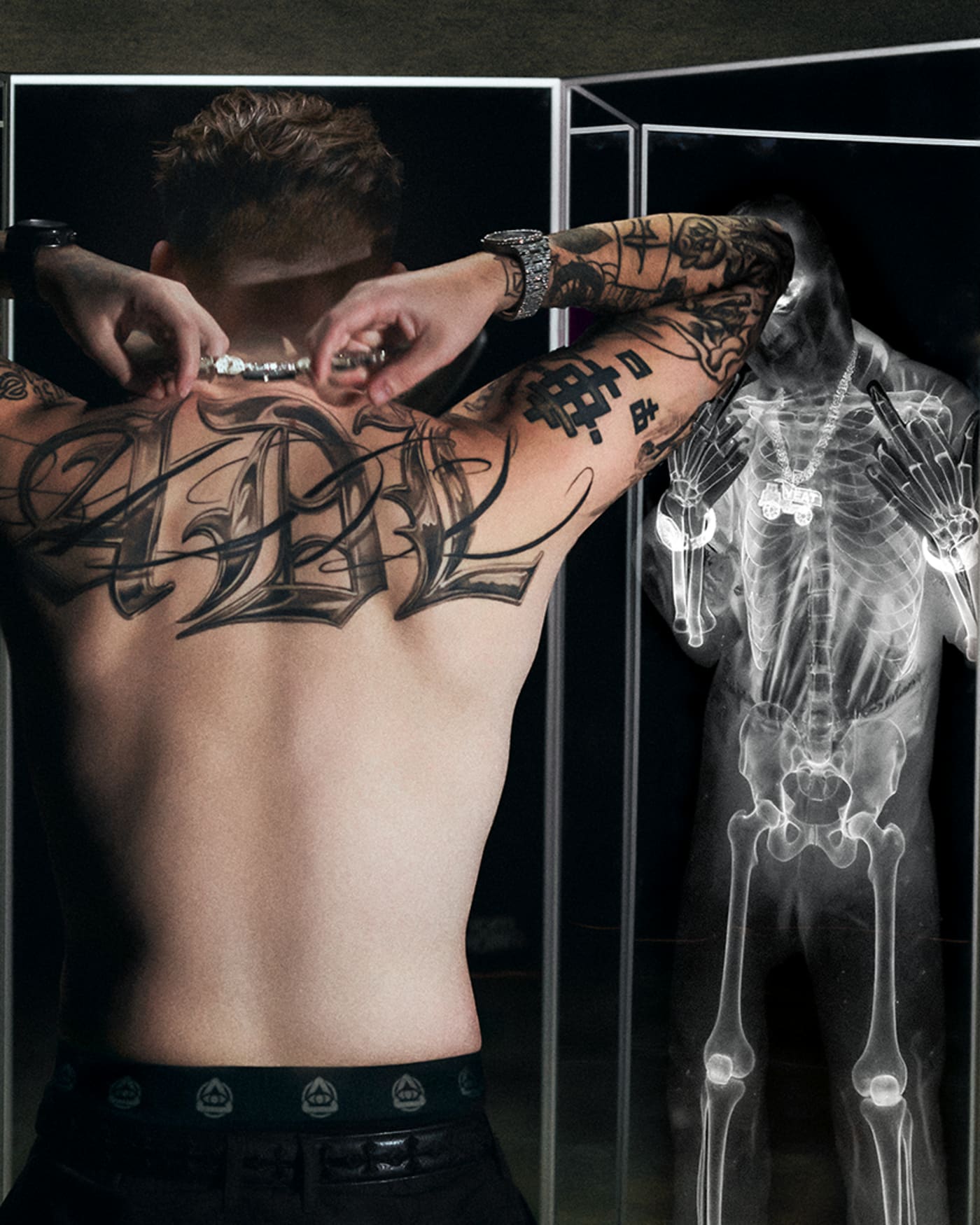 A shirtless man with tattoos stands in front of mirrors, surrounded by three men in streetwear and an X-ray reflection.