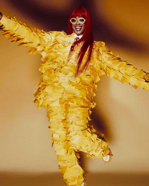 Person in a vibrant yellow ruffled outfit with red glasses poses joyfully
