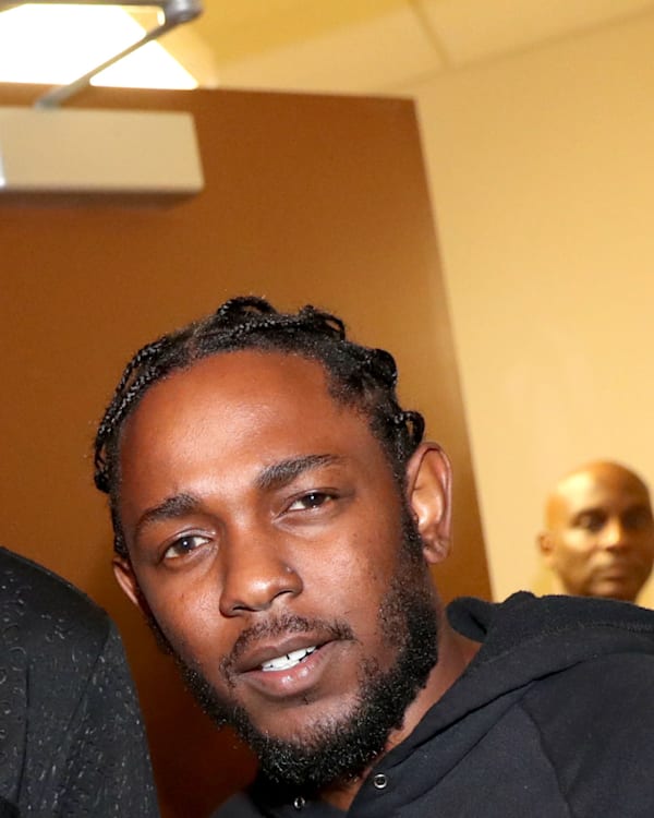 Snoop Dogg and Kendrick Lamar smiling together indoors, with another person in the background.