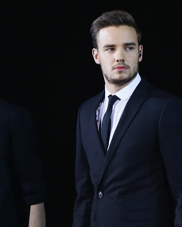 Zayn Malik and Liam Payne in formal attire, standing side by side against a dark background.