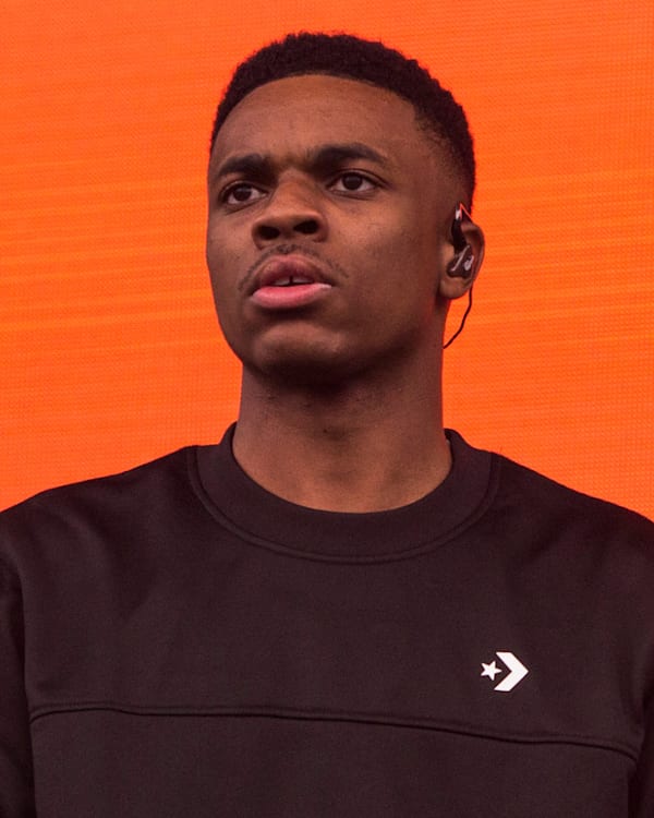 A person wearing a black sweatshirt with an orange background, looking forward with an earpiece.