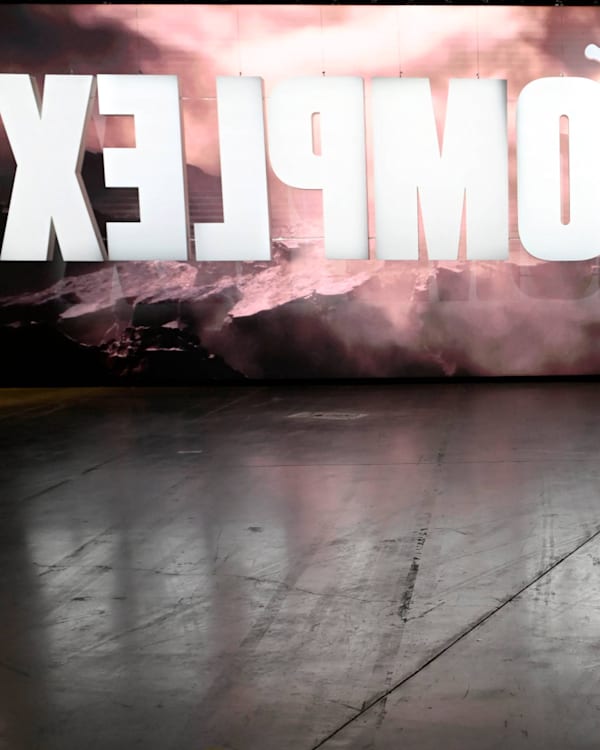 A large illuminated sign reads "COMPLEX CON" in a convention center, with people walking nearby.