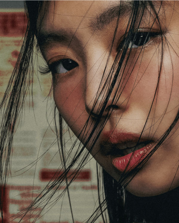 A person with long black hair and wind-swept strands, looking intently at the camera. The background has posters with red text. jennie complex cover