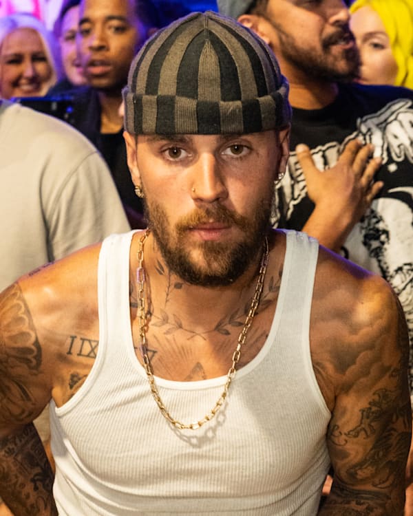 Justin Bieber in a striped cap and white tank top is surrounded by a crowd at an event.