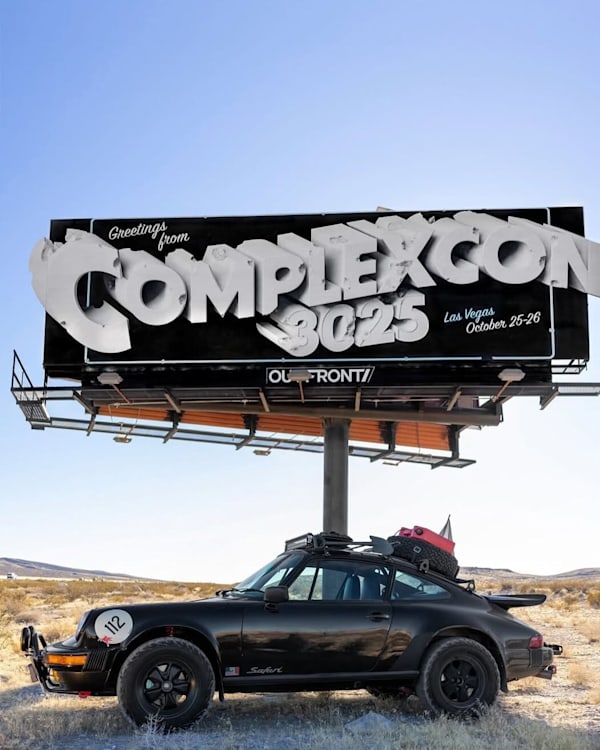 A black vintage Porsche with luggage on top is parked under a billboard for "ComplexCon 3025" in Las Vegas, October 25-26.
