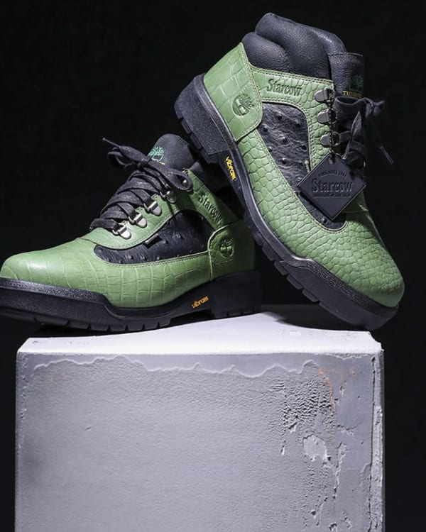 A pair of green and black sneakers with a textured pattern, displayed on a concrete pedestal against a dark background.