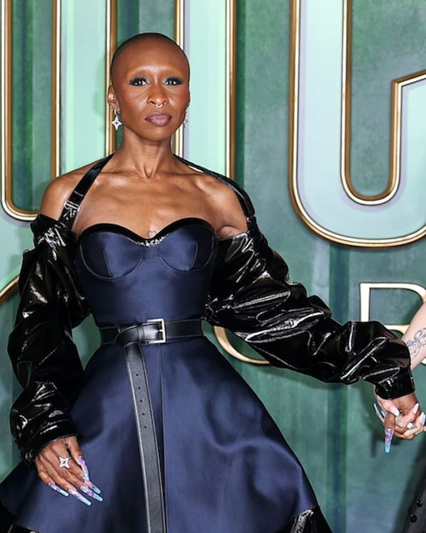 Cynthia Erivo and Ariana Grande holding hands at an event, both wearing elegant black dresses.