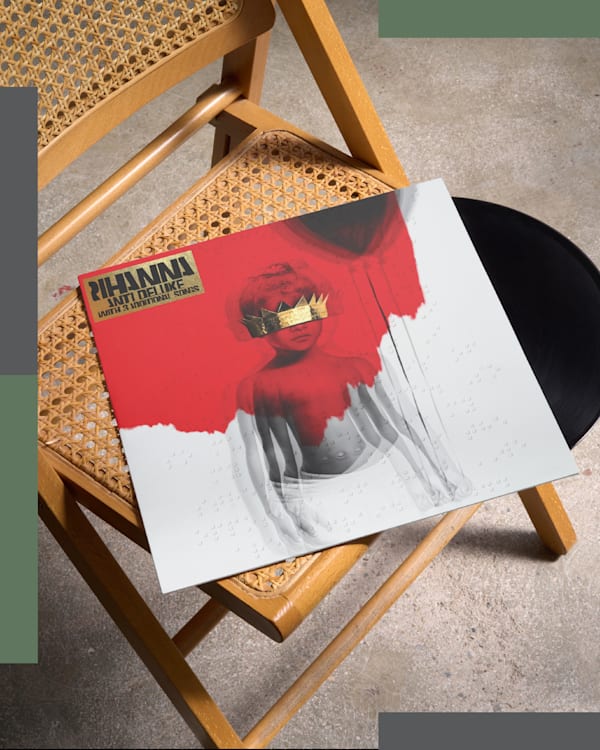 Two vinyl records: Rihanna's "Anti" on a chair, and another with a red cover and pixelated artwork leaning against a wall.