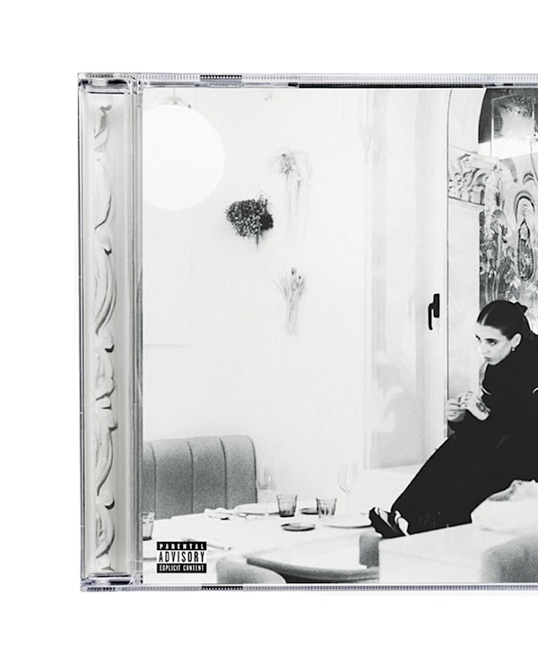A black and white album cover featuring a person sitting on a couch in a modern, minimalistic room with large windows.