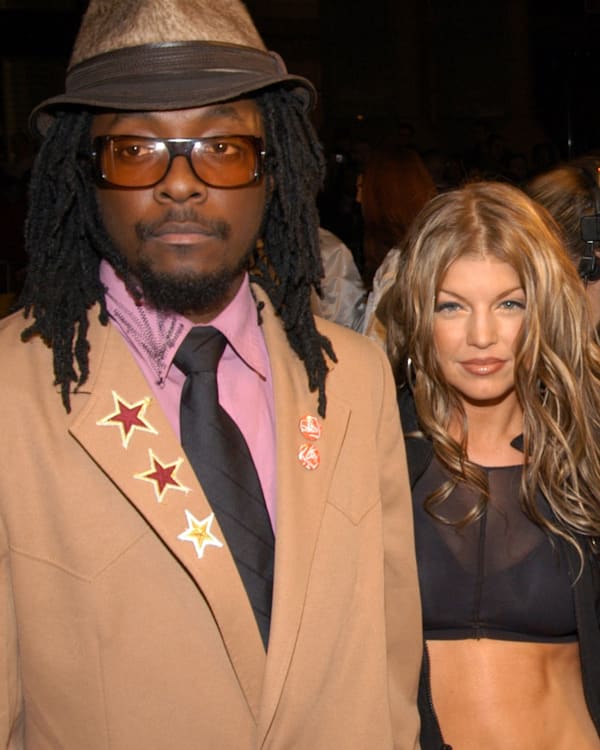 The Black Eyed Peas: will.i.am in a tan suit, Fergie in a black top, apl.de.ap in a gray hat, and Taboo in a white outfit and hat.