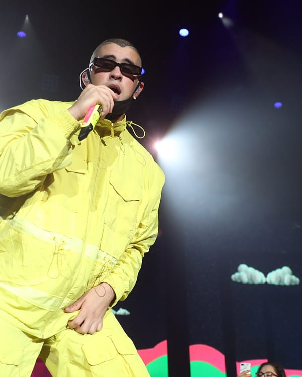 Bad Bunny in a yellow outfit and J Balvin in a black tank top perform on stage with microphones, under colorful lights.