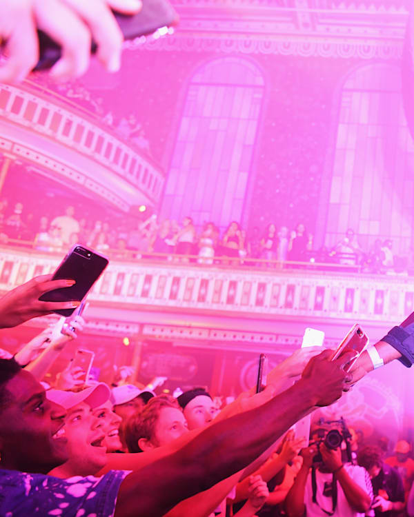 Mike WiLL Made-It in sunglasses interacts with fans at a vibrant, pink-lit concert. The audience eagerly takes photos in a grand venue. Mike WiLL Made-It was one of the great rap producers of the 2010s, here is a ranking of all of his songs.