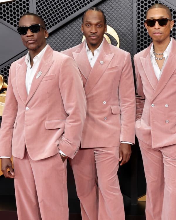 Clipse in matching pink suits and sunglasses pose on a red carpet at an event with a geometric black and gold backdrop, Pharrell too