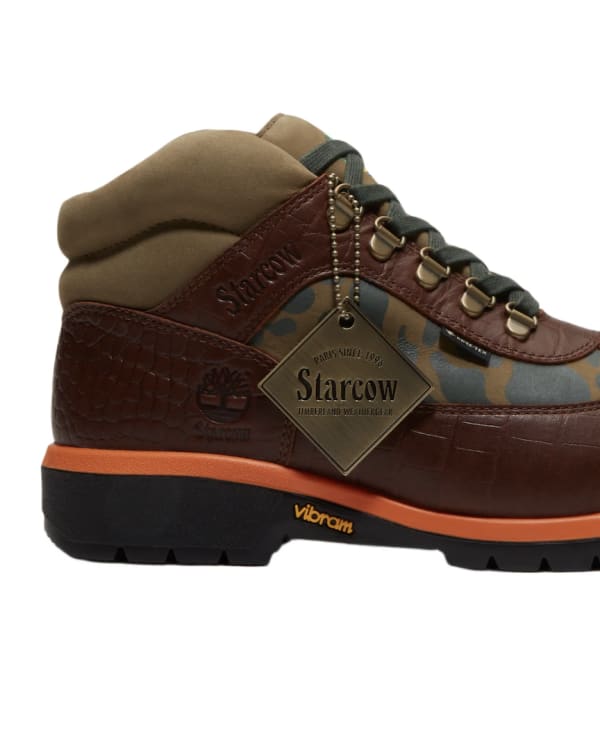 A brown and tan hiking boot with orange accents, featuring a camo pattern and a "Starcow" tag. Vibram sole branding visible.