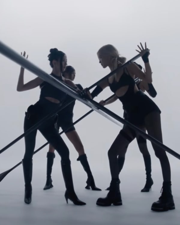 Four women in black outfits striking dynamic poses with large oars in a minimalist, white studio setting for a new BLACKPINK video