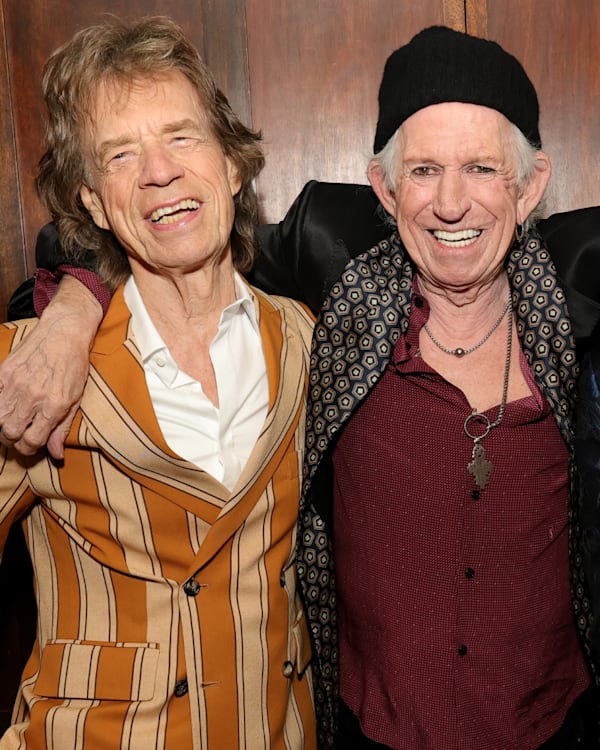Mick Jagger, Keith Richards, and Ronnie Wood smiling together, wearing stylish jackets.