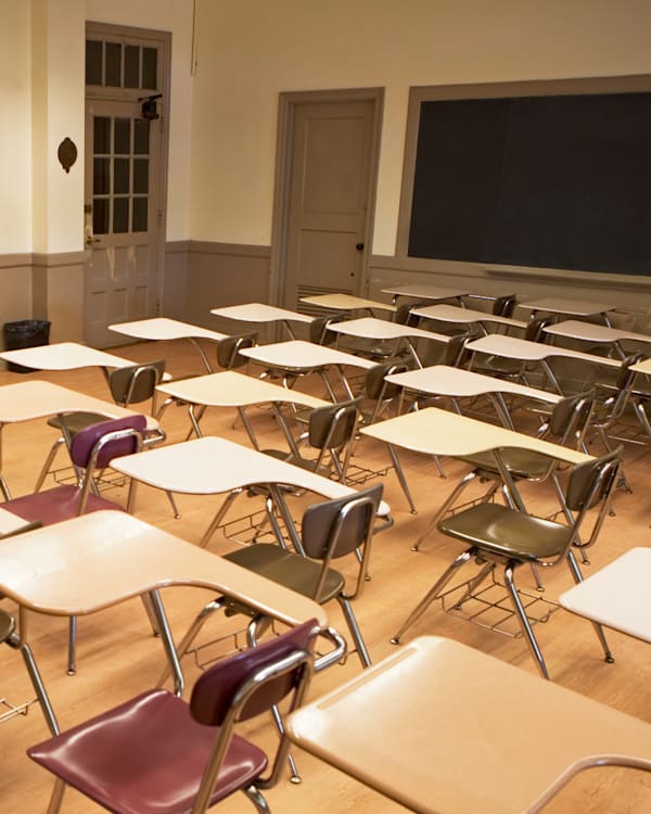 Empty classroom with rows of desks and chairs, a whiteboard at the front, and a wooden floor.