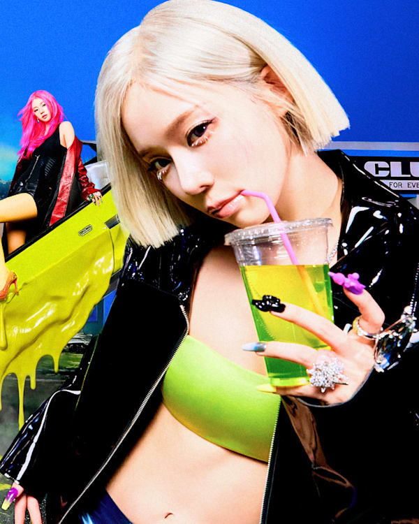 aespa members with colorful hair in a vibrant, surreal setting. One is holding a drink, others pose with a shopping cart and on a slide.