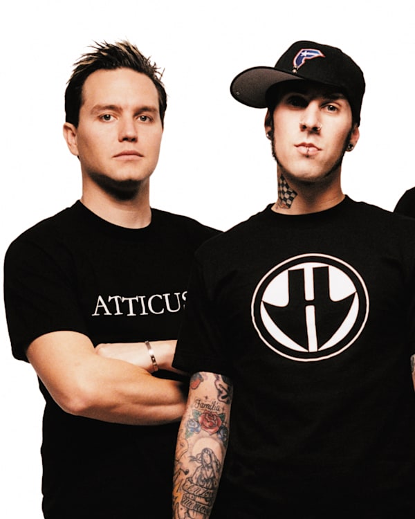 blink-182, dressed in black shirts, stand against a white background. Travis Barker in center wears a cap and has tattoos.