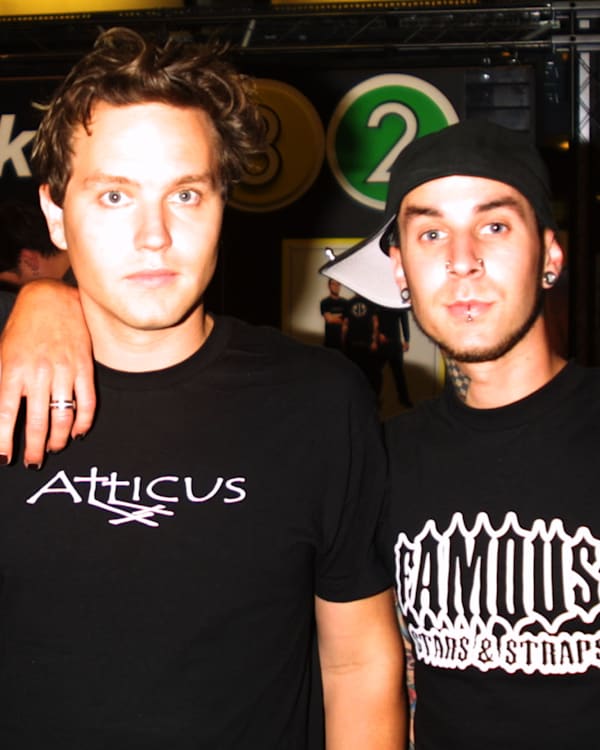 Members of Blink-182, Tom DeLonge, Mark Hoppus, and Travis Barker, pose together in casual attire at an event.