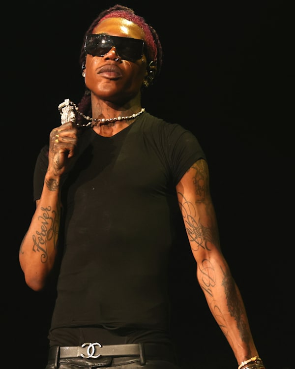 Destroy Lonely wearing sunglasses and a black t-shirt holds a microphone on stage.
