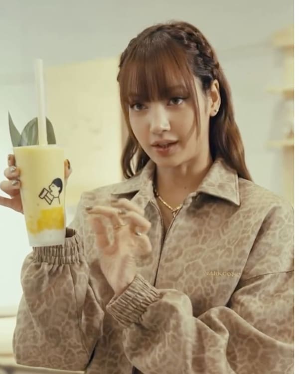 Lisa from BLACKPINK holding a bubble tea cup with a drawing of her on it, next to an illustrated drink with fruits.