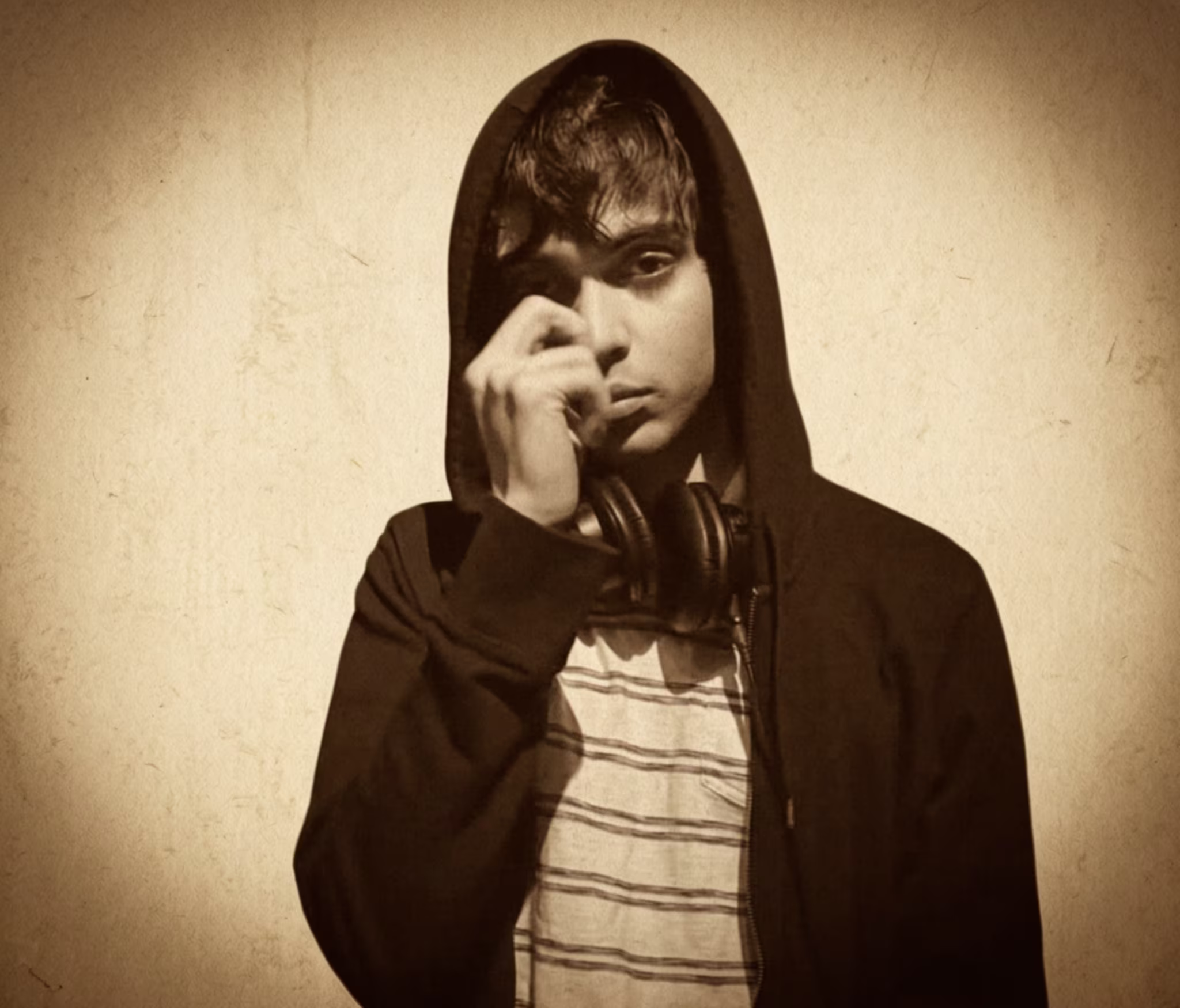 twentythree in a hoodie and striped shirt, wearing headphones around their neck, poses against a plain background.
