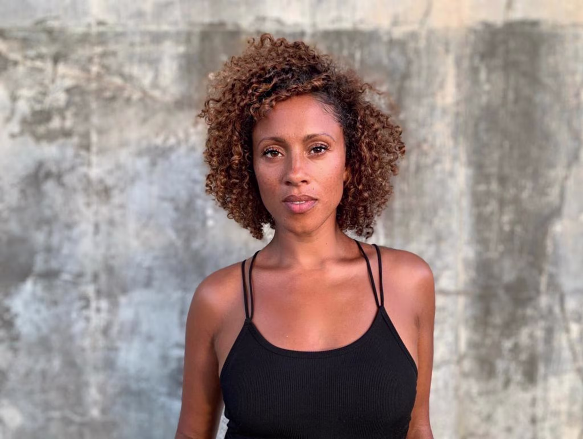 Tiana Canterbury stands against a grey wall wearing a black top