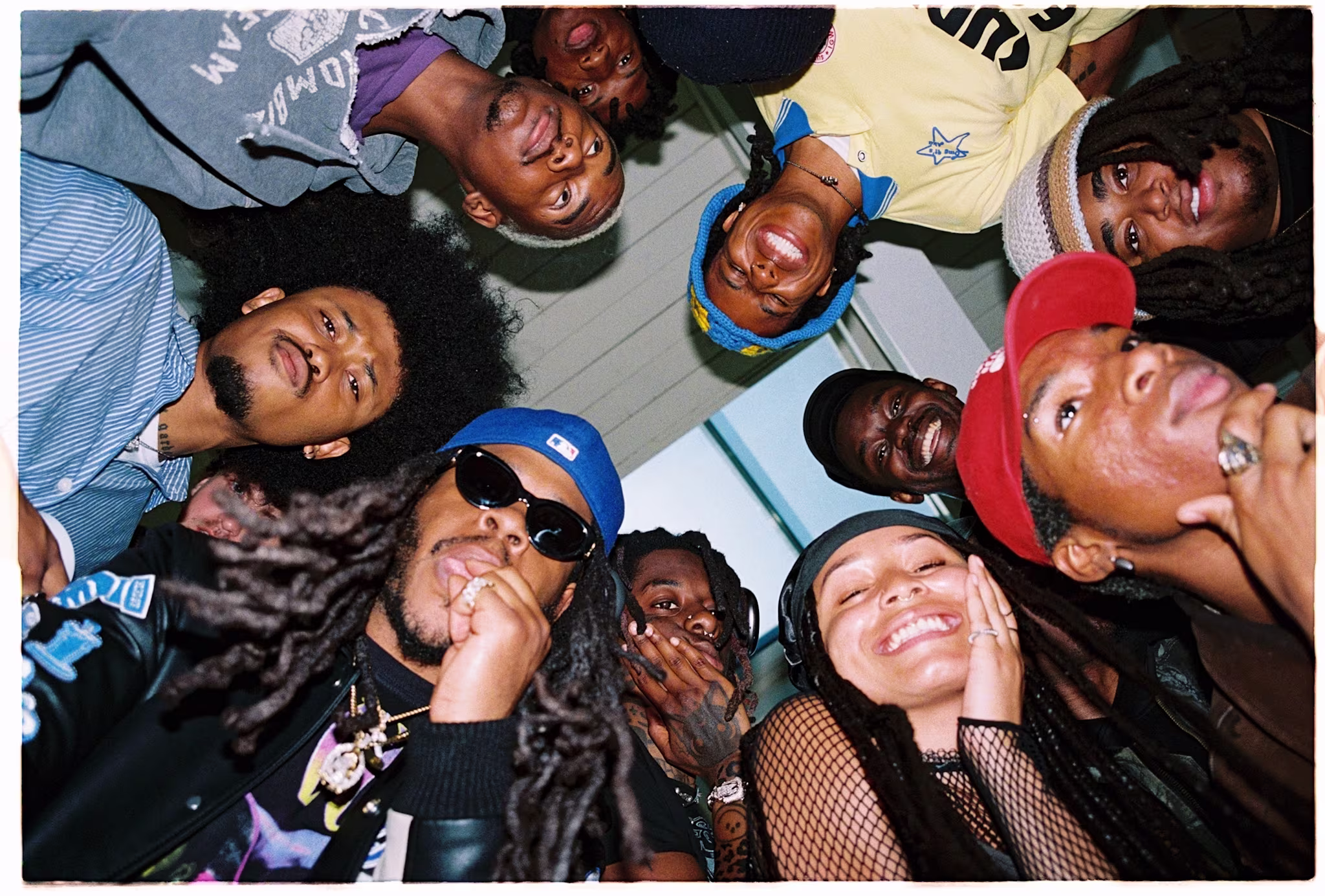 A group of people looking down at the camera, smiling and posing. They are wearing casual clothing and hats, with one person in sunglasses.