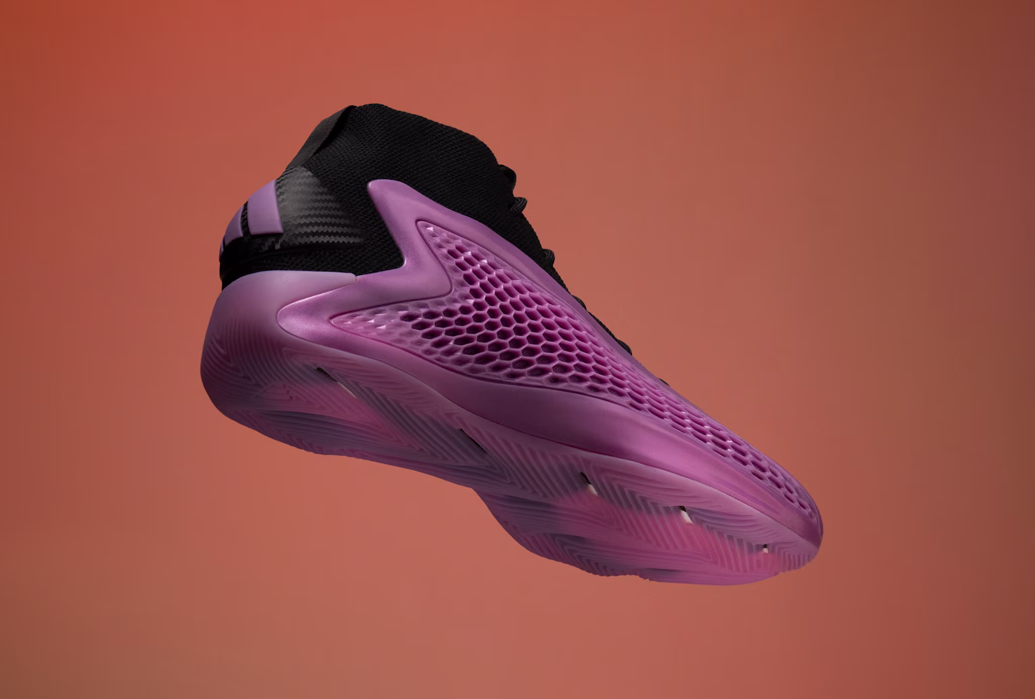 A black and purple athletic shoe with a textured sole and mesh design, set against a gradient orange background.