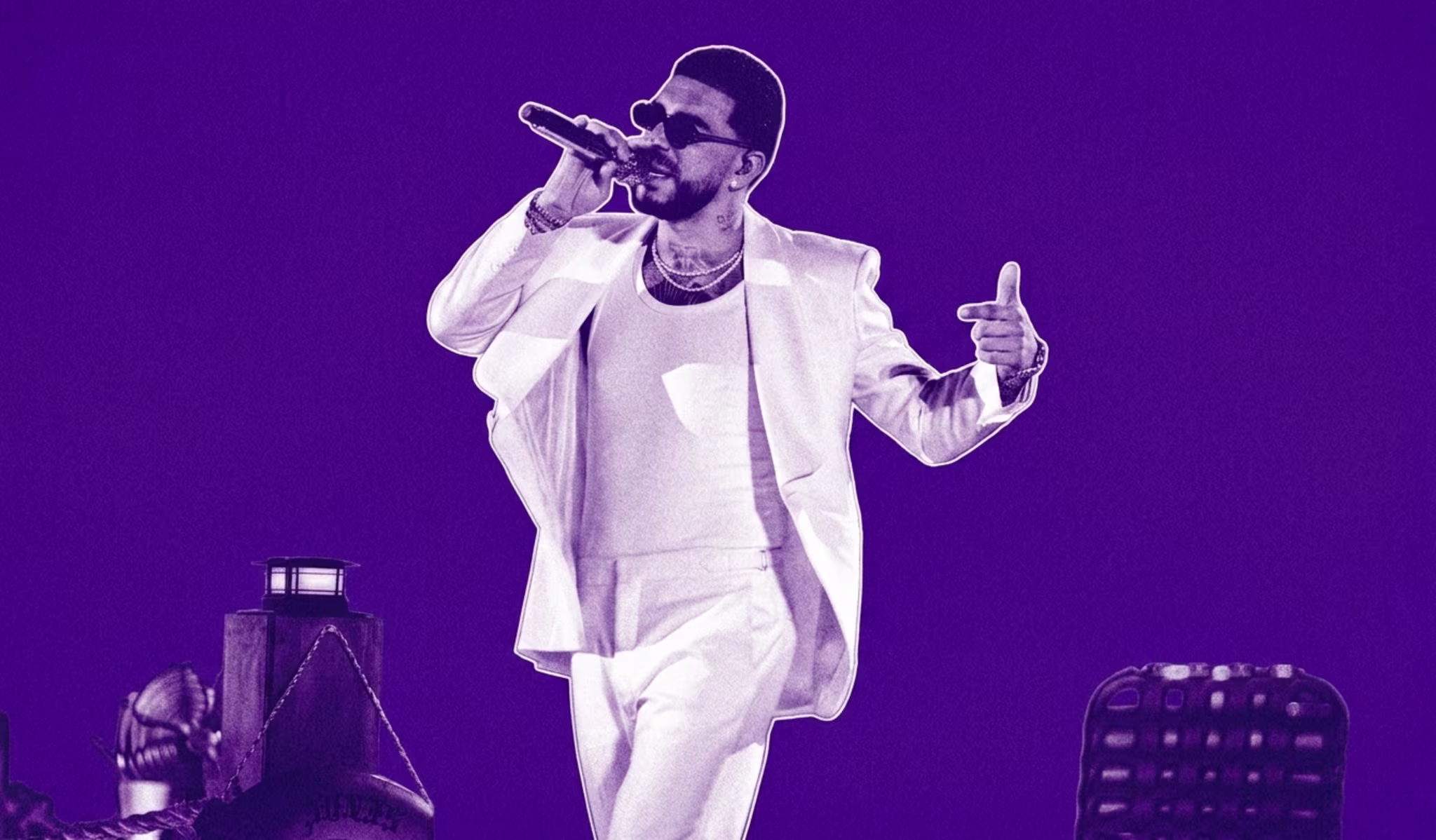 Ryan Castro in a white suit and sunglasses performs on stage with a microphone, set against a purple background.