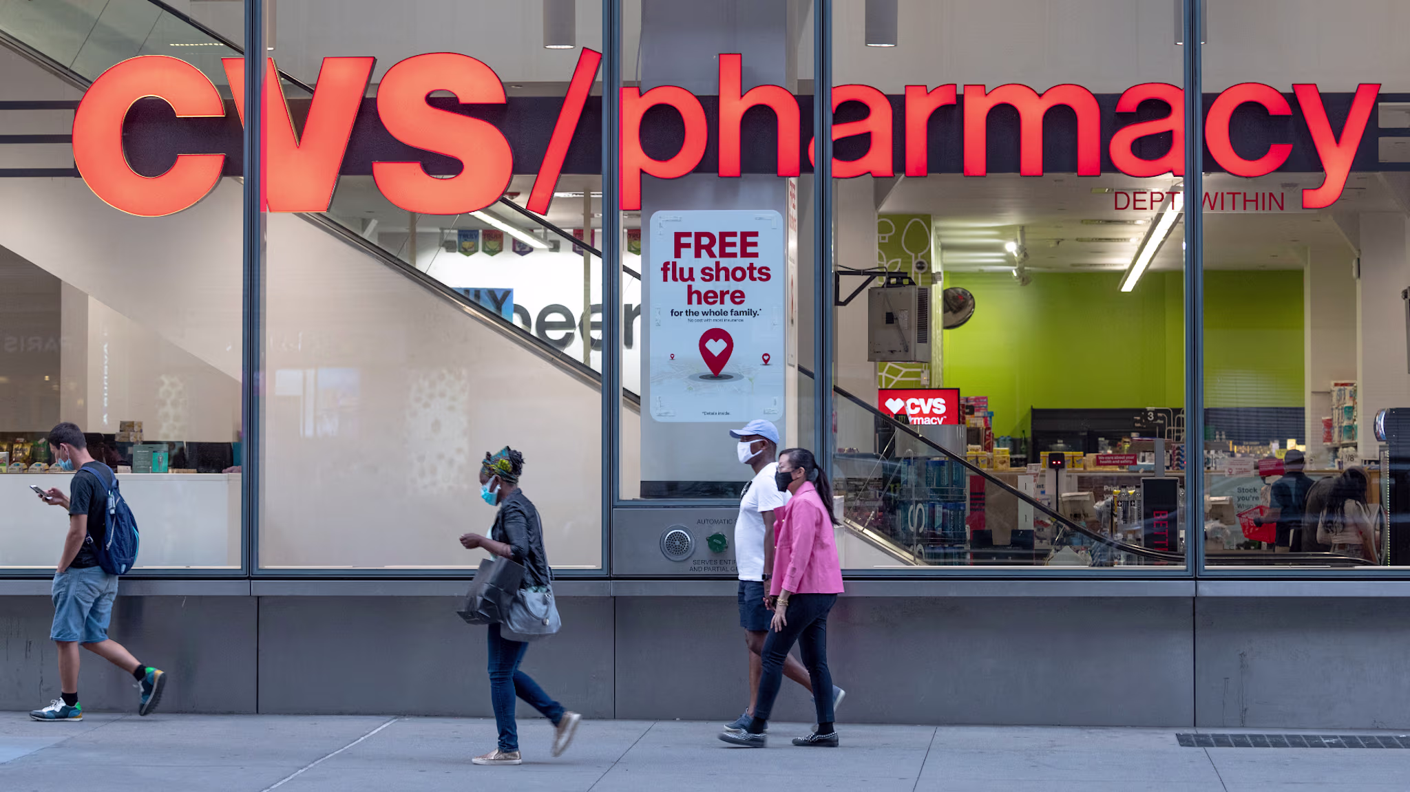 People wearing masks walks past a CVS Pharmacy.