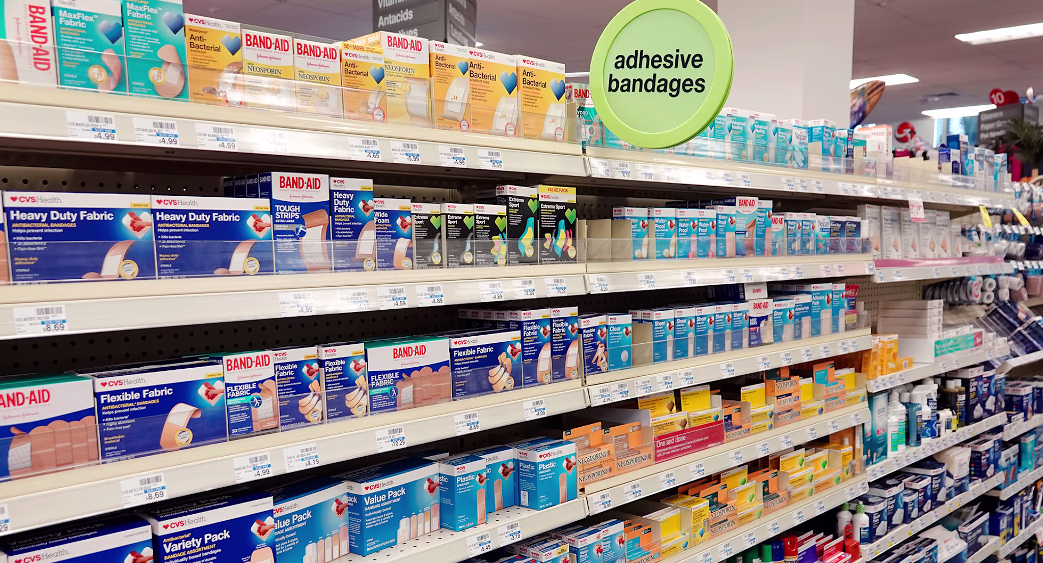 Shelves stocked with various boxes of adhesive bandages in a store aisle under a sign that says "adhesive bandages"
