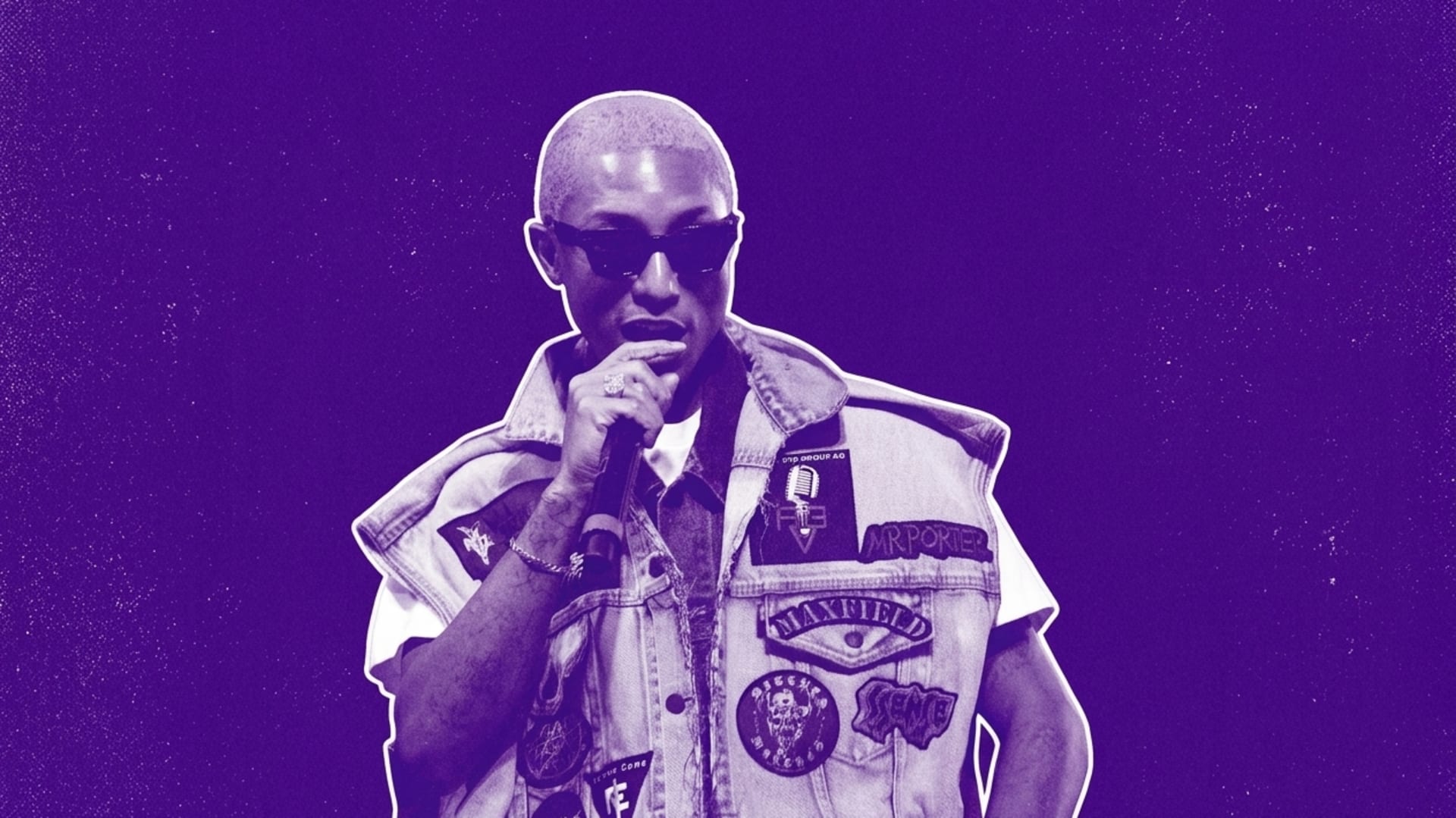 Pharrell with short hair and sunglasses, wearing a patch-covered denim vest, holding a microphone against a purple background.