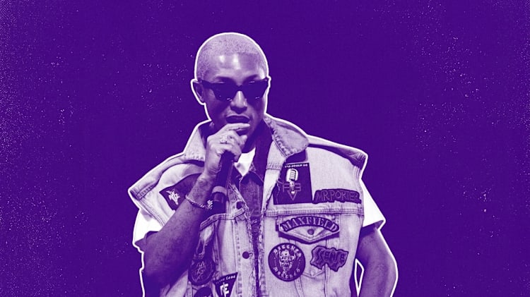 Pharrell with short hair and sunglasses, wearing a patch-covered denim vest, holding a microphone against a purple background.