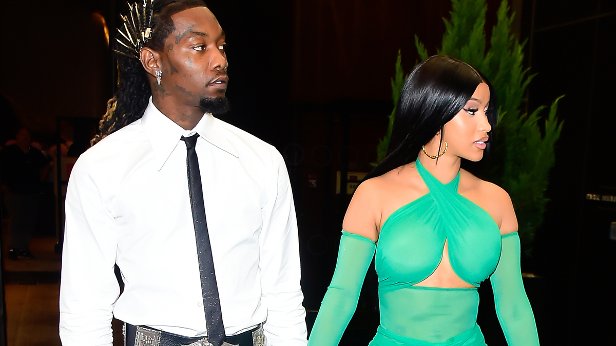 Offset and Cardi B walking together, Offset wearing a white shirt and black pants, Cardi B in a stylish, sheer green dress