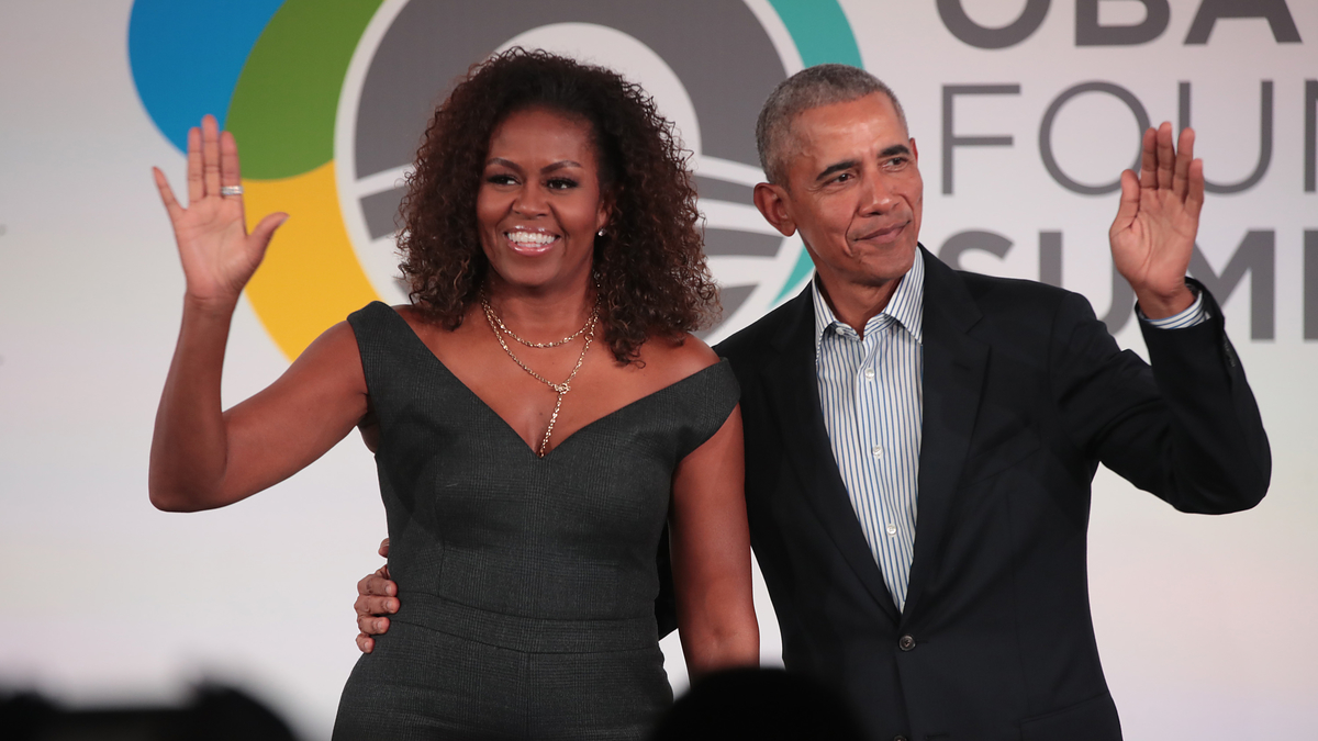 Barack Obama in a suit and Michelle Obama in a stylish off-shoulder dress wave at the Obama Foundation Summit