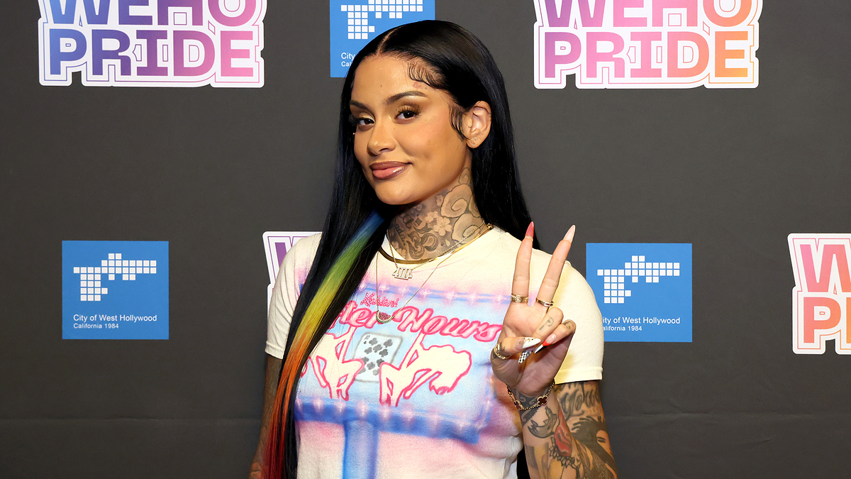 Kehlani poses with a peace sign at a WEHO PRIDE event, wearing a graphic t-shirt