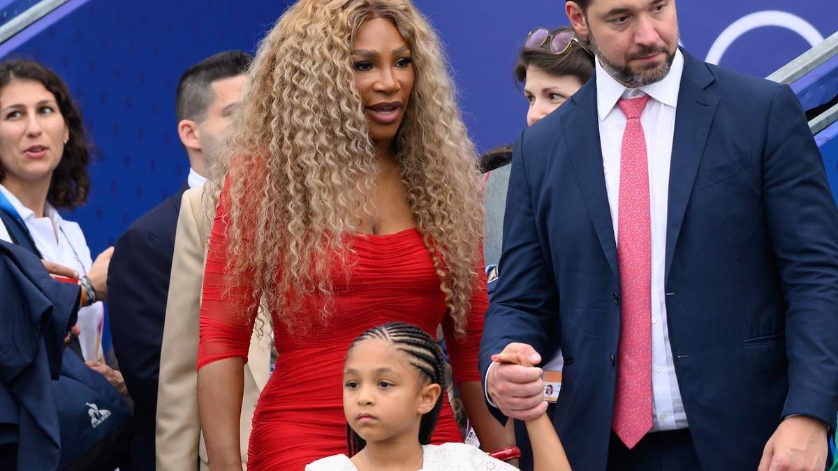 Serena Williams in a form-fitting dress with Alexis Ohanian and their daughter, Alexis Olympia Ohanian Jr., holding hands while being surrounded by people