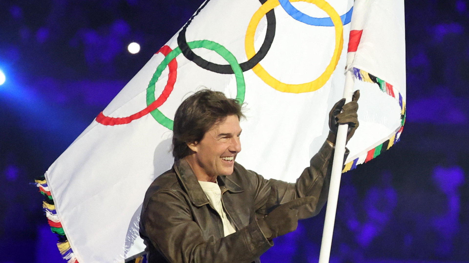 Tom Cruise waving the Olympic flag during closing ceremony.