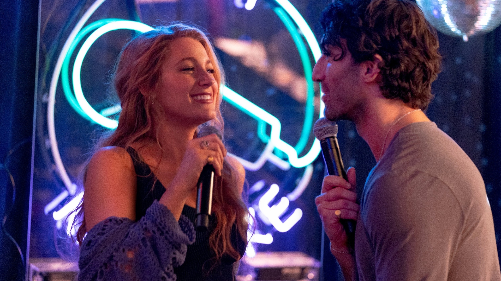 Lily Bloom (Blake Lively, left) and Ryle Kincaid (Justin Baldoni, right) stare at each other with microphones in their hands in what appears to be a karaoke bar.