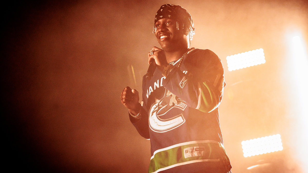 Lil Yachty performs on stage wearing a Vancouver Canucks jersey with a bandana, holding a microphone, and smiling