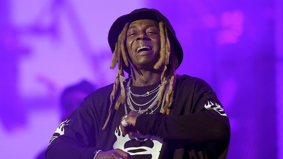 Lil Wayne performs on stage, wearing a patterned shirt and a bucket hat