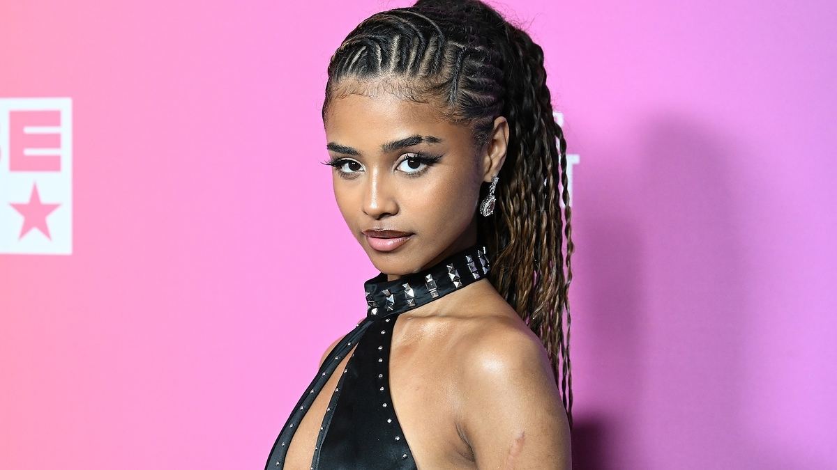 Unknown woman on red carpet wearing a halter-style dress with studded detailing, standing in front of a pink backdrop