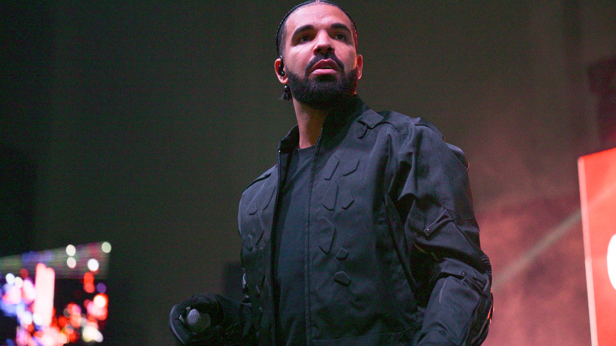 Drake performs on stage wearing a black outfit, holding a microphone, with a focused expression