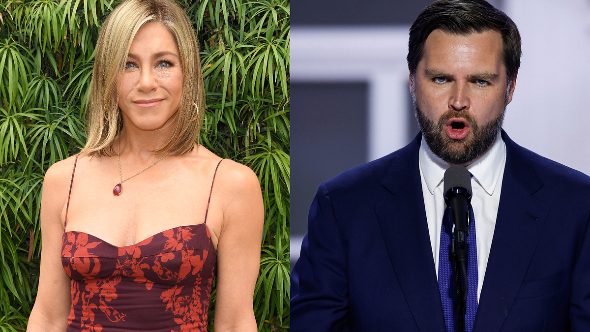Jennifer Aniston in a sleeveless floral dress stands beside a man in a blue suit and tie speaking at a podium