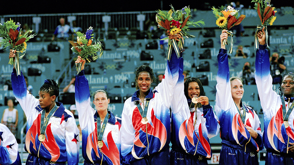 Five athletes, each holding a bouquet and wearing medals and matching tracksuits, celebrate their win at the Atlanta 1996 Olympic Games