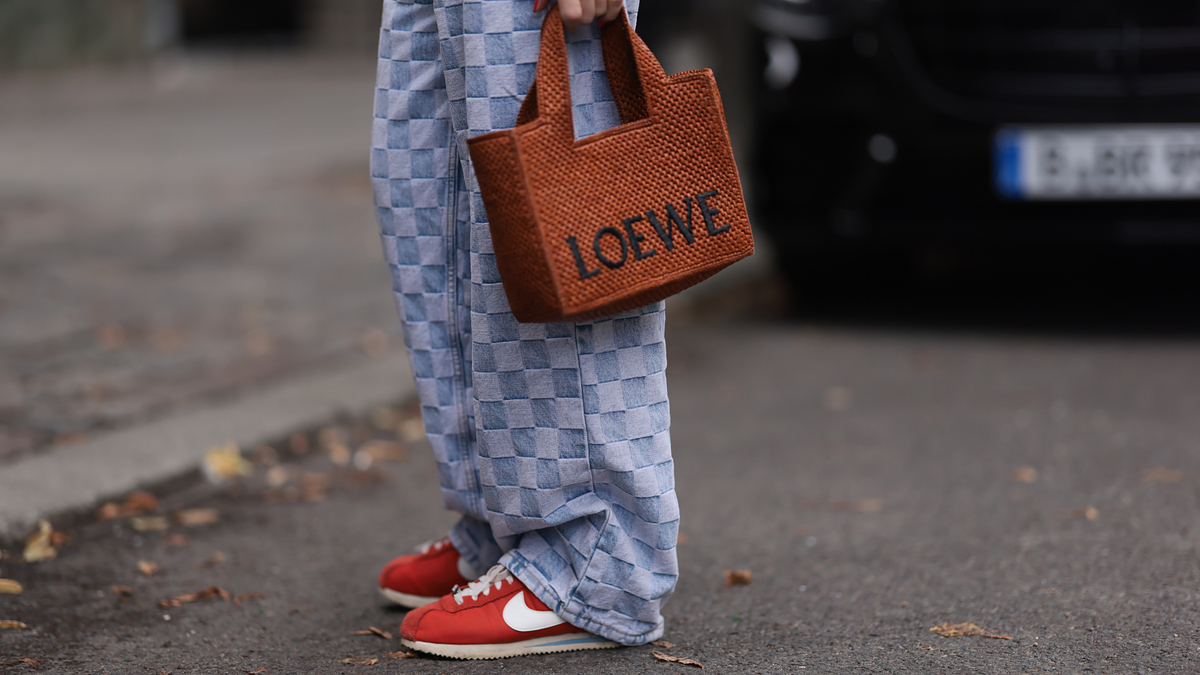 Person wearing loose-fitting checkered pants, red Nike sneakers, and carrying a Loewe handbag