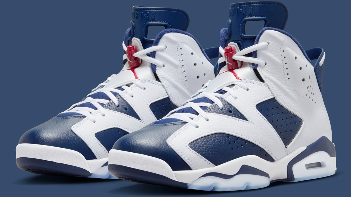 A pair of white and navy blue high-top sneakers with red accents and white laces, displayed on a plain blue background